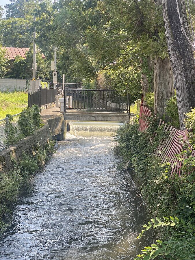 Small irrigation canal in Azumino with bridge and rural vegetation, ideal for cycling