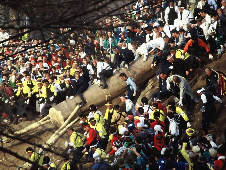 Onbashira festival log being dropped down a hillside with riders on top